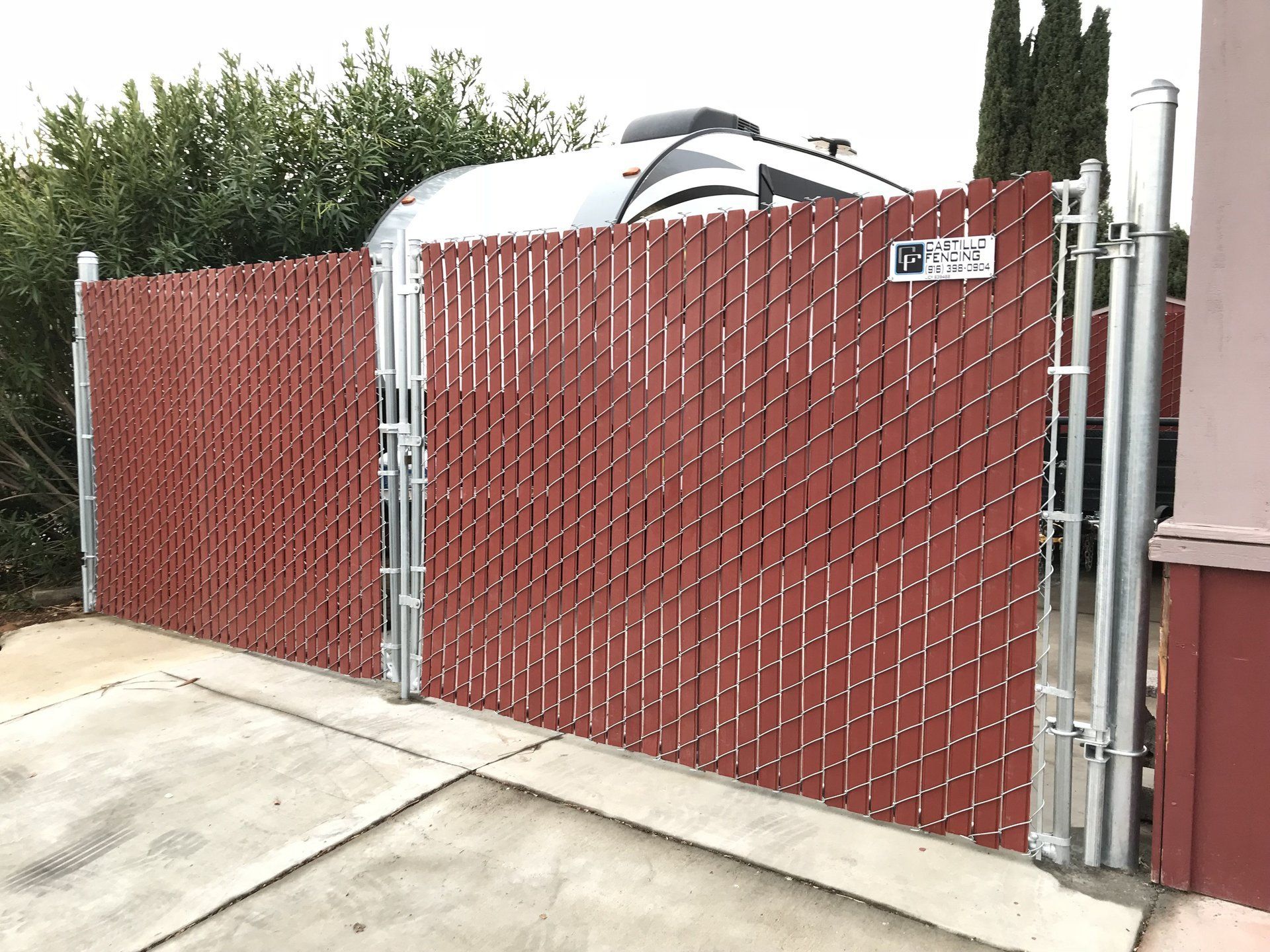 a red chain link fence with a gate and a rv parked behind it .