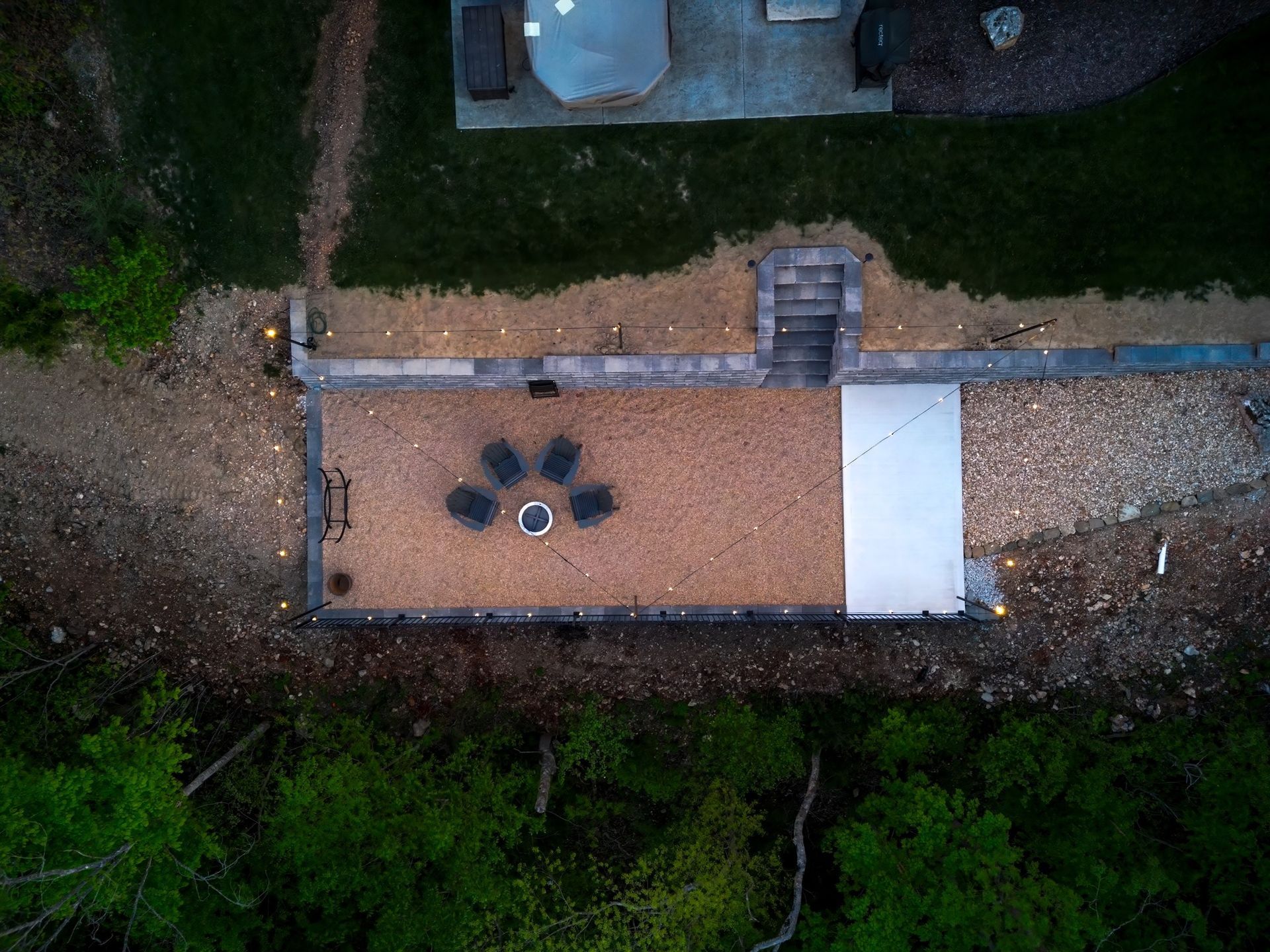 An aerial view of a patio with a fire pit and chairs surrounded by trees.