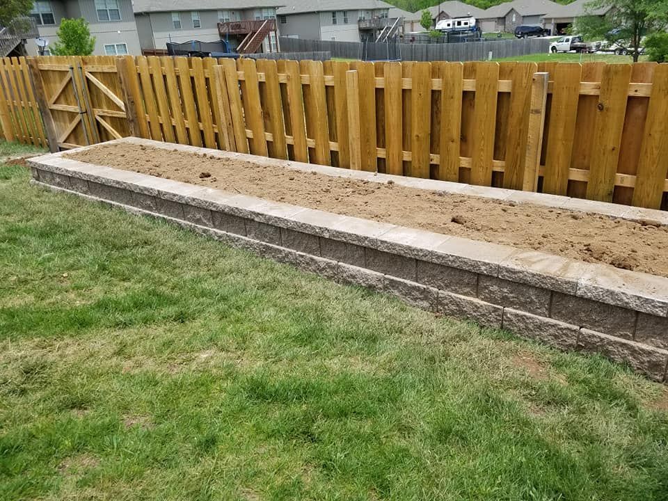 A wooden fence surrounds a garden bed in a backyard.