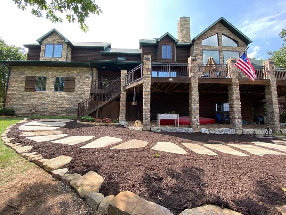 A large stone house with a large deck and an american flag in front of it.