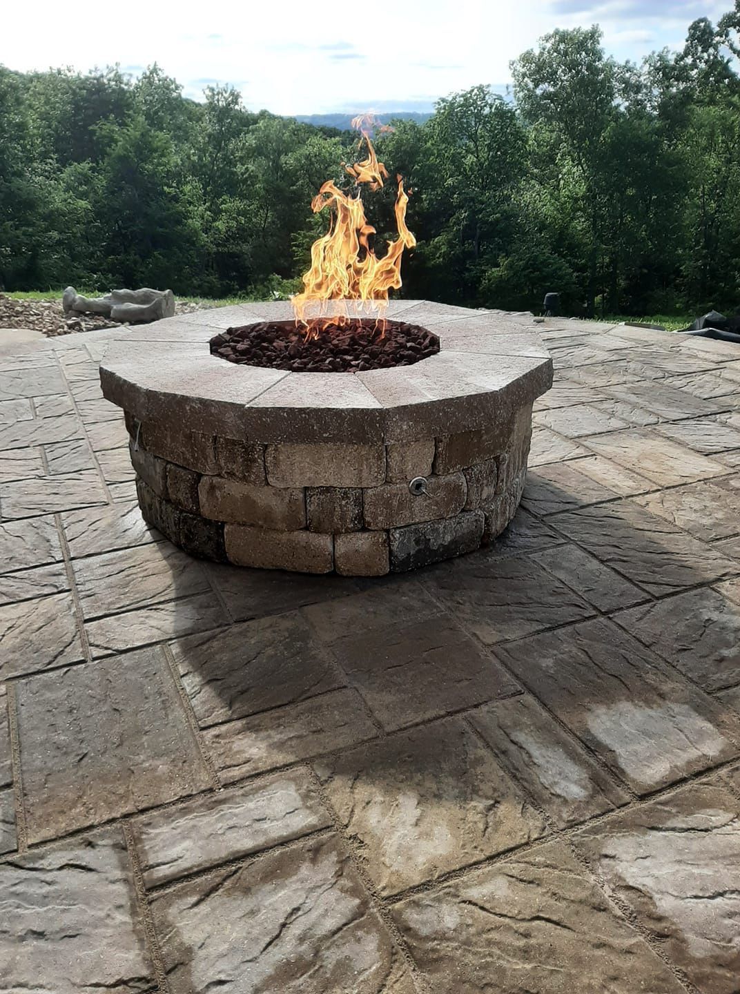 A fire pit is sitting on a patio with trees in the background.