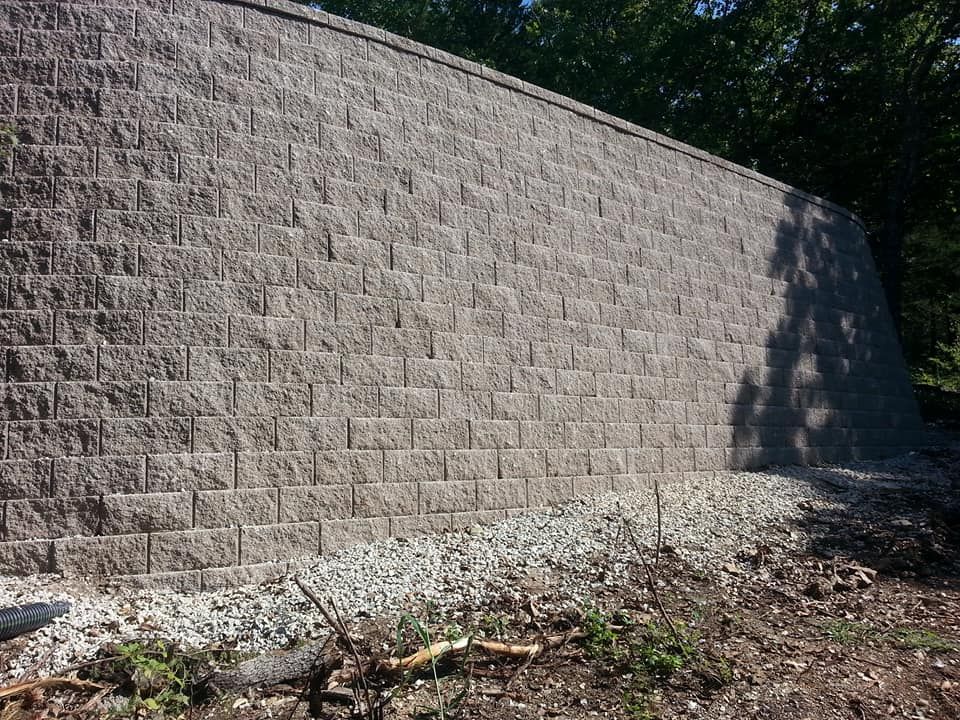 A large brick wall is surrounded by gravel and trees.