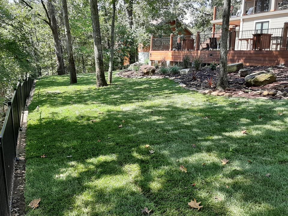A large lush green lawn in front of a house surrounded by trees.