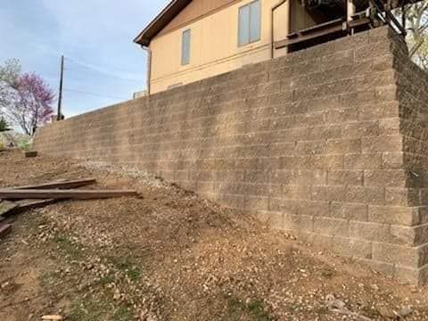 A large brick wall is sitting on top of a hill next to a house.