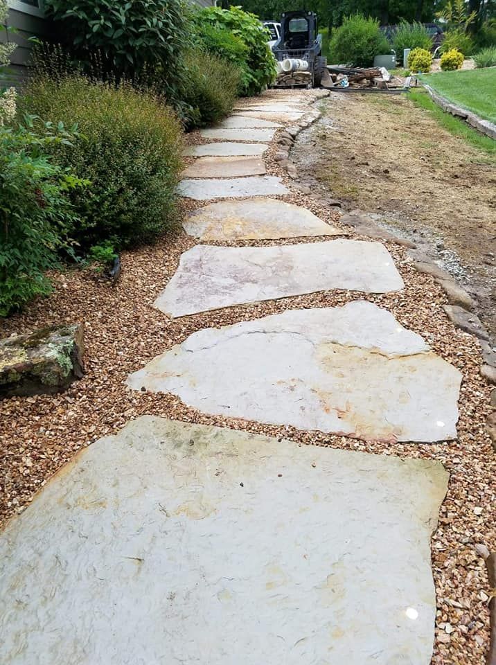 A stone walkway going through a garden with a bulldozer in the background.