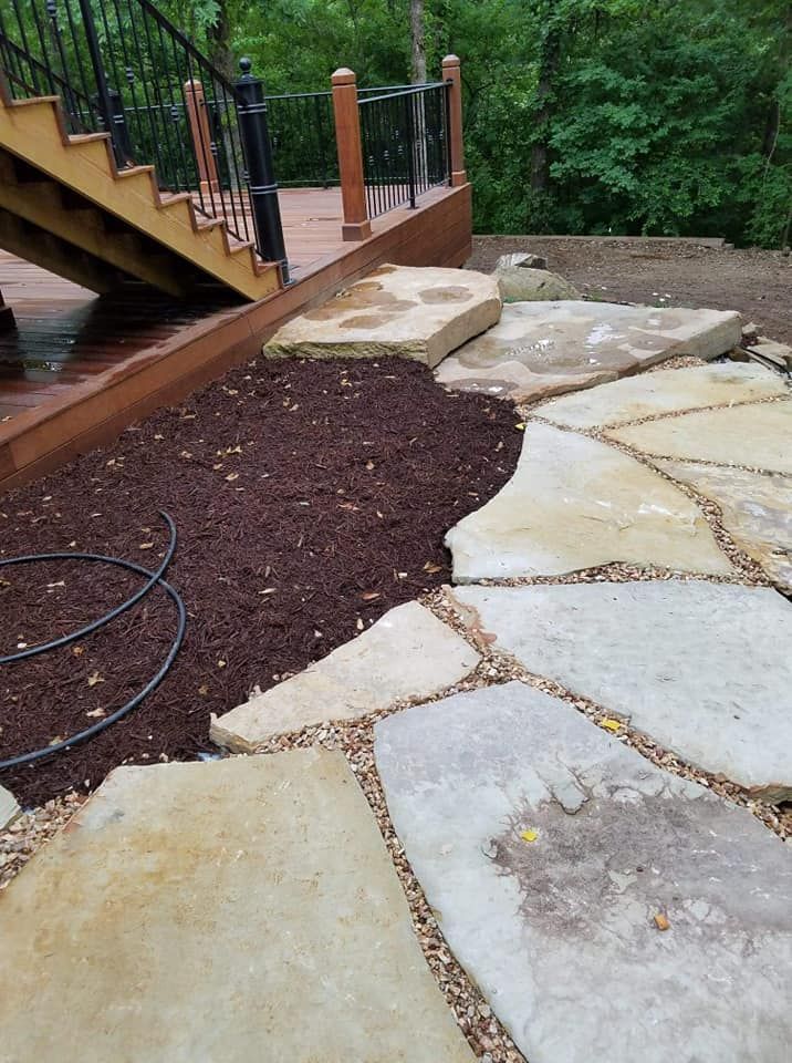 A stone walkway leading to a deck with stairs in the background.