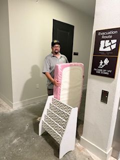 A man is carrying a mattress and a bookshelf in a hallway.