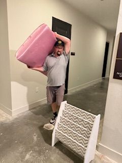 A man is carrying a pink suitcase on his head in a hallway.