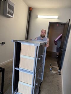 A man is carrying a dresser in a hallway.