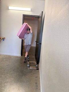 A man is carrying a pink box on his head in a hallway.