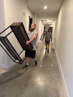 A man is carrying a table down a hallway while another man holds a ladder.