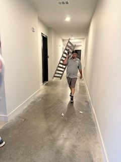 A man is carrying a ladder down a hallway.