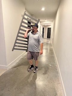 A man is carrying a crib in a hallway.