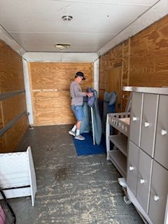 A man is standing in the back of a trailer holding a mattress.