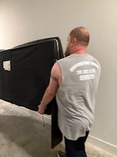 A man in a gray tank top is carrying a large piece of furniture.