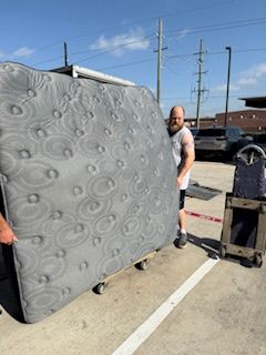A man is holding a large mattress in a parking lot.