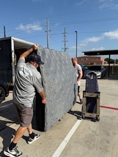 A man is carrying a large mattress in a parking lot.