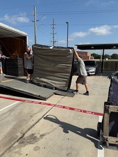 Two men are lifting a mattress out of a truck in a parking lot.