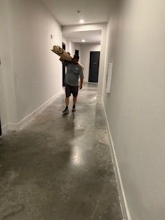 A man is carrying a large piece of wood down a hallway.