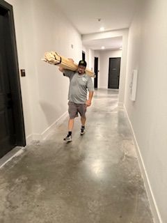 A man is carrying a large piece of wood down a hallway.