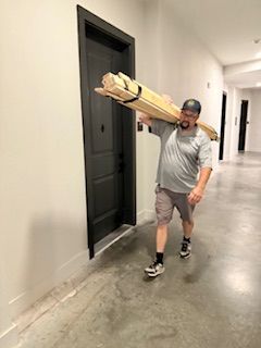 A man is carrying a large piece of wood in a hallway.