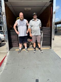 Two men are standing on the back of a truck.