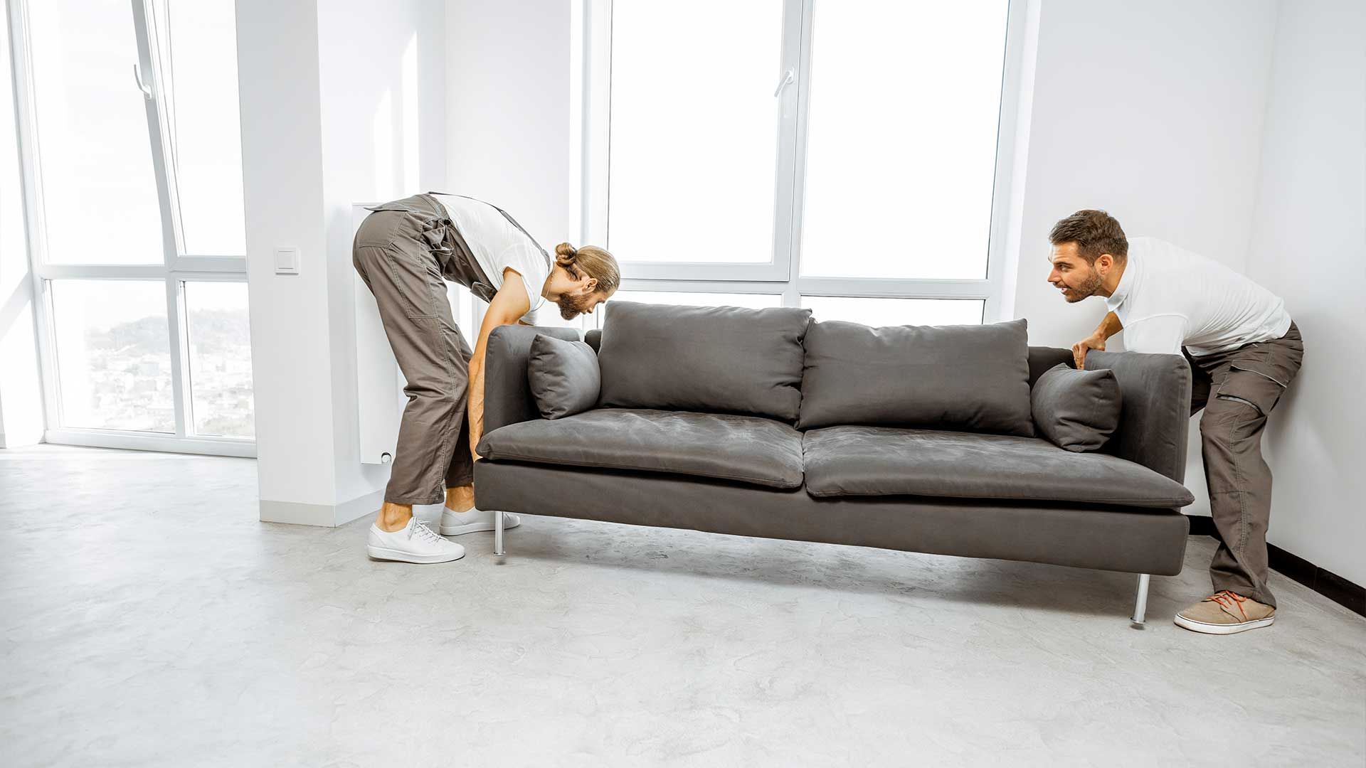 Two men are moving a couch in a living room.