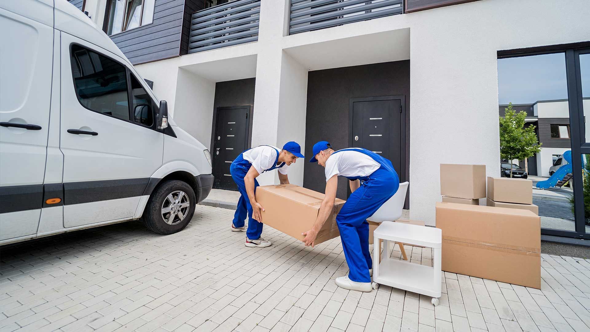 Two movers are carrying a box in front of a van.