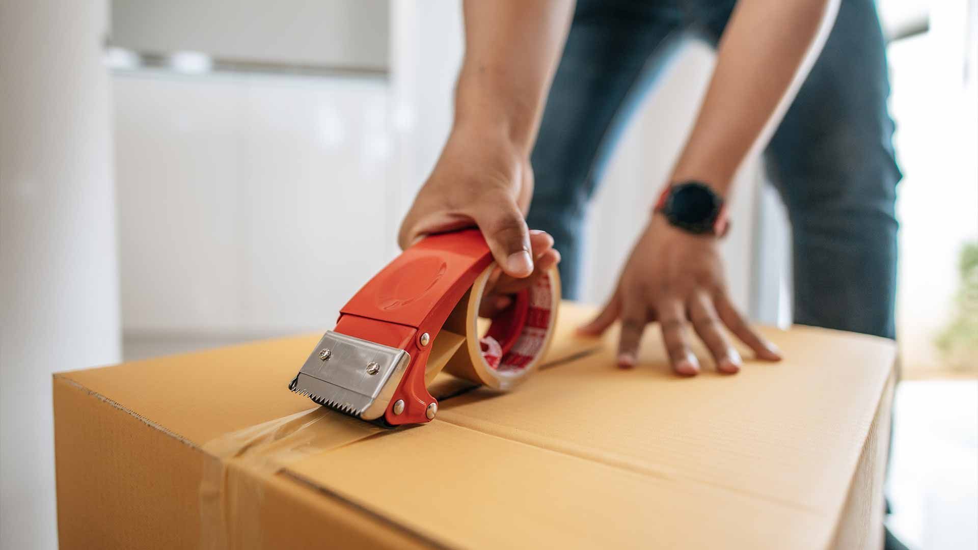 A person is taping a cardboard box with tape.