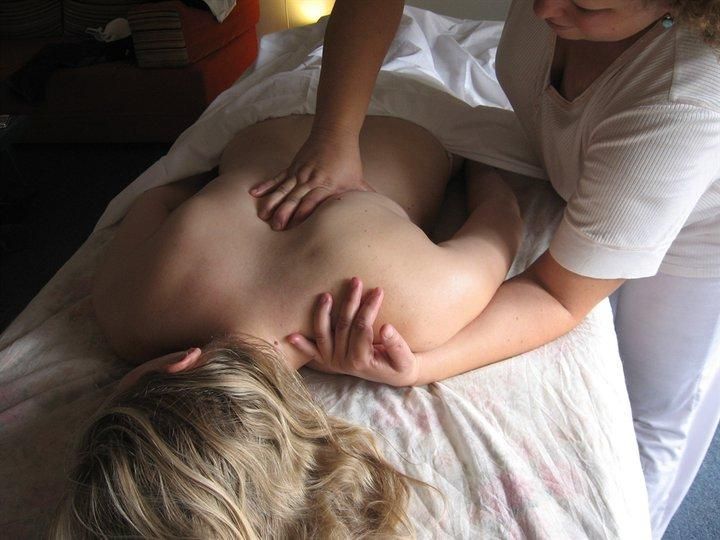 A woman receiving a back massage on a bed, with a white towel and dim indoor lighting