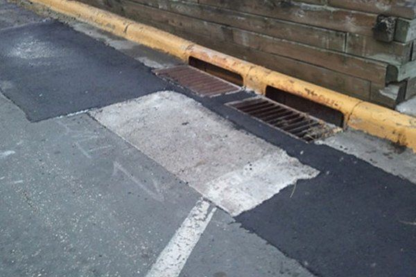 A drain on the side of a road next to a yellow curb