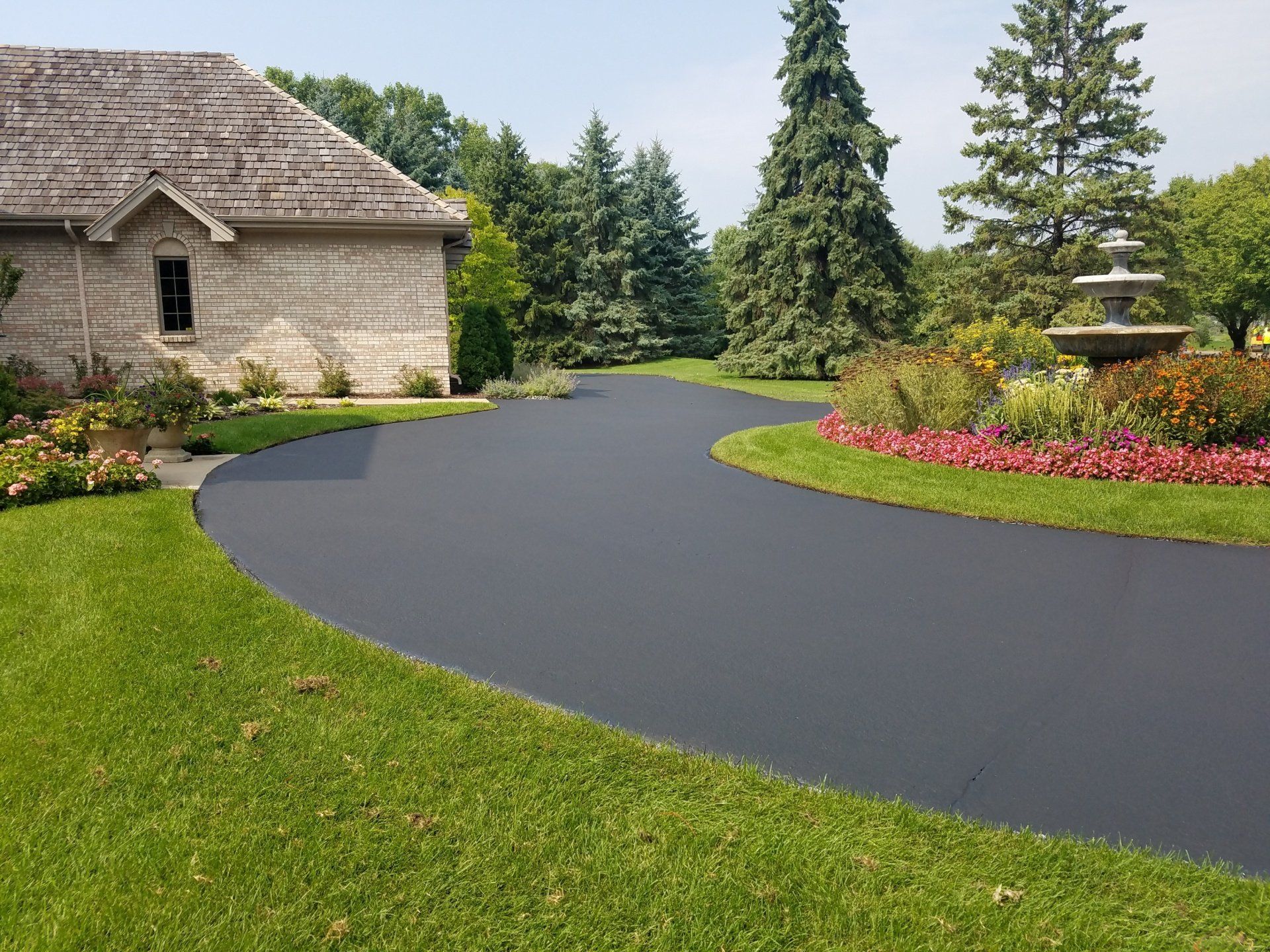 A driveway leading to a house with a fountain in the middle of it.