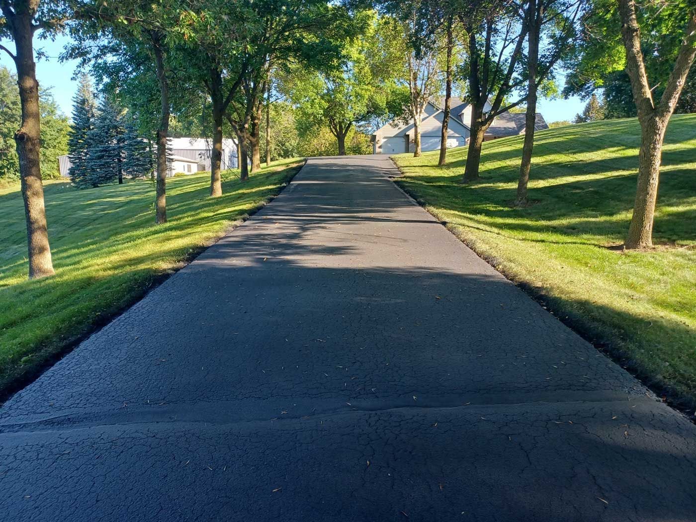A driveway leading to a house surrounded by trees and grass.