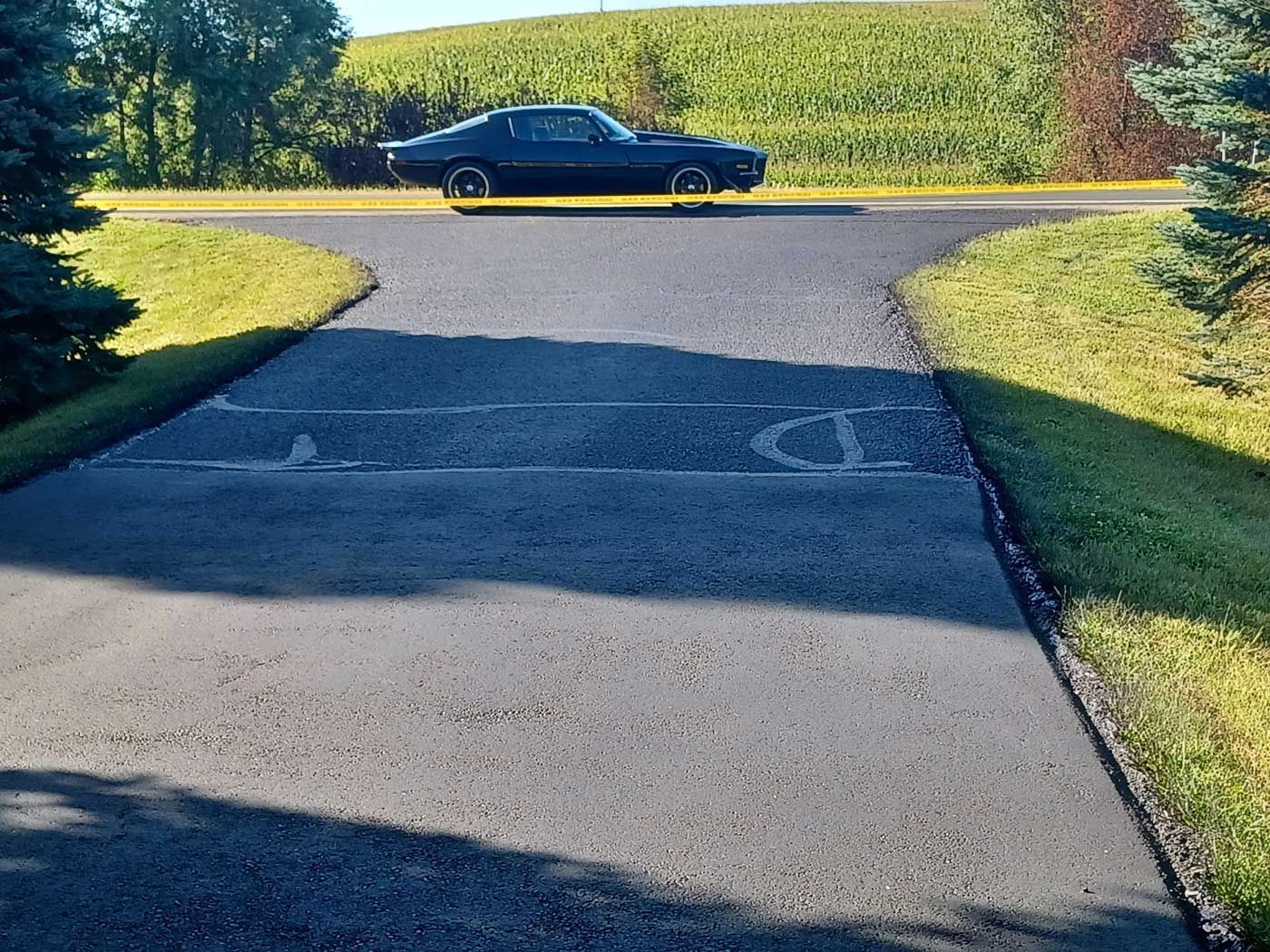 A black car is driving down a road next to a grassy hill.