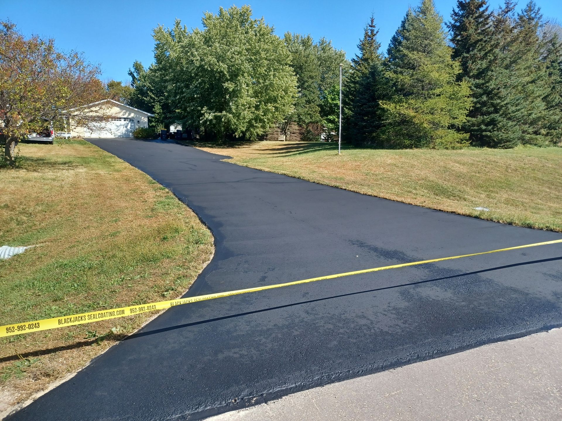 A newly paved driveway is surrounded by grass and trees.