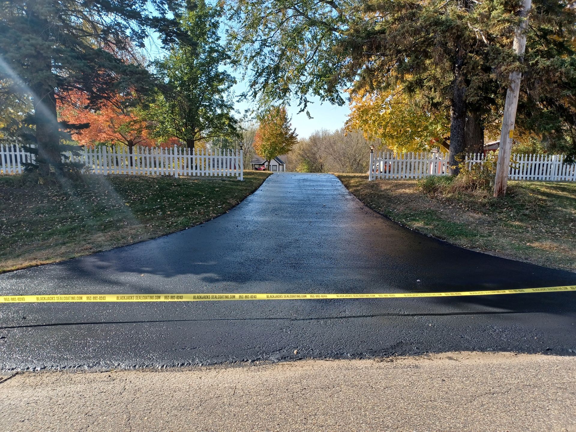 A newly paved driveway with a yellow tape along the side of it.