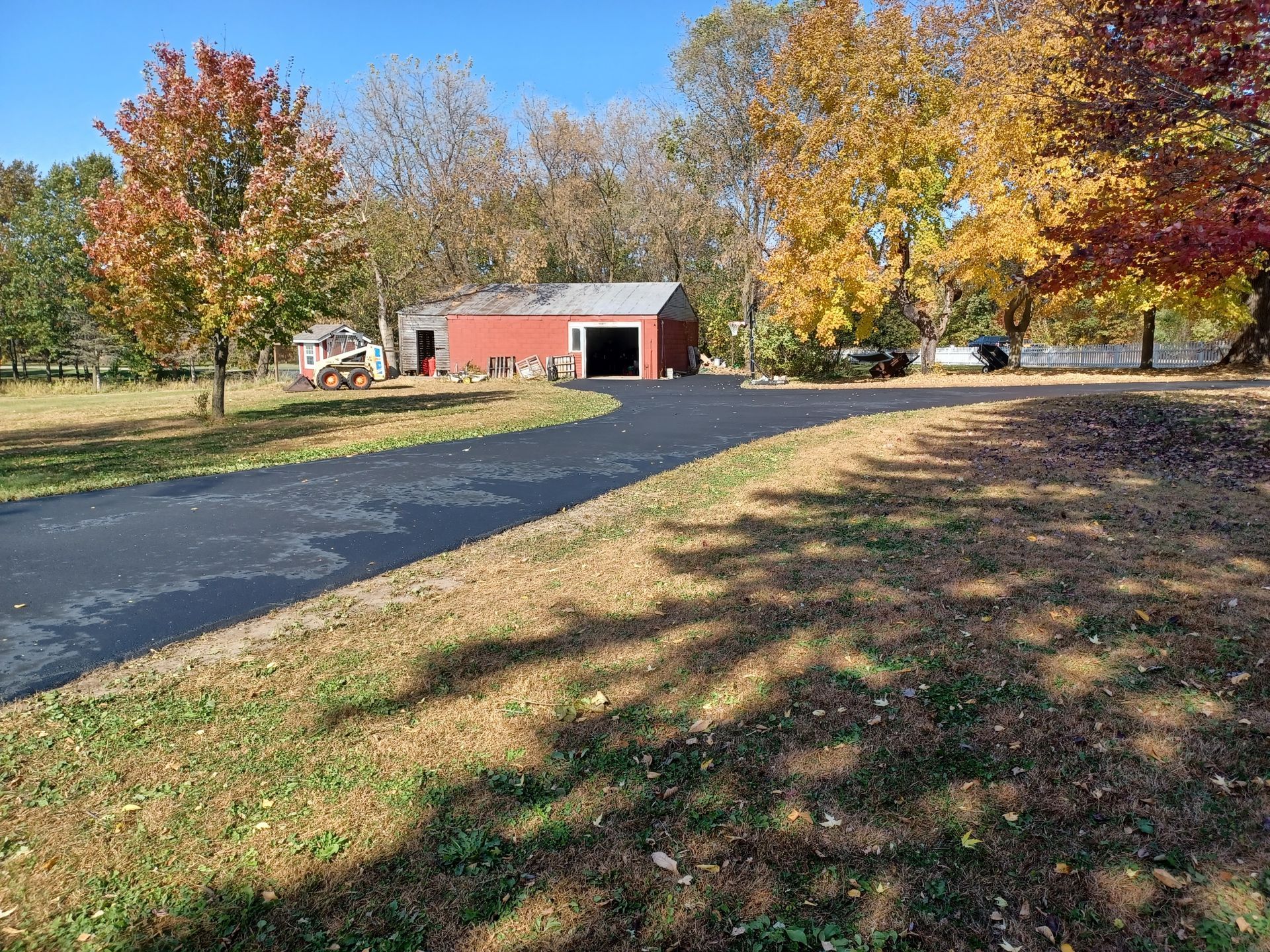 A driveway leading to a red barn surrounded by trees on a sunny day.