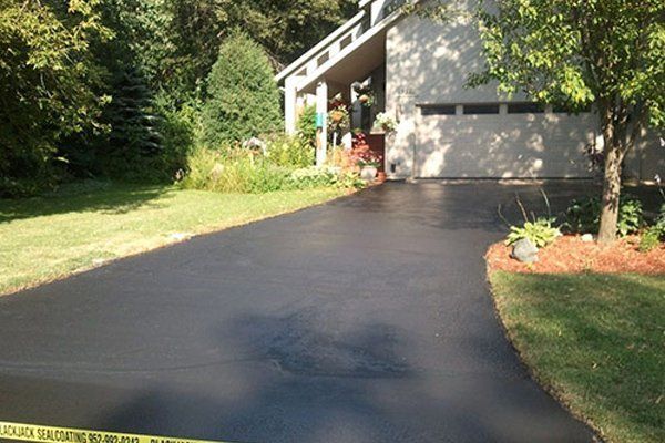 A black driveway leading to a house with trees in the background