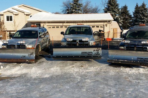 Three snow plows are parked in front of a house