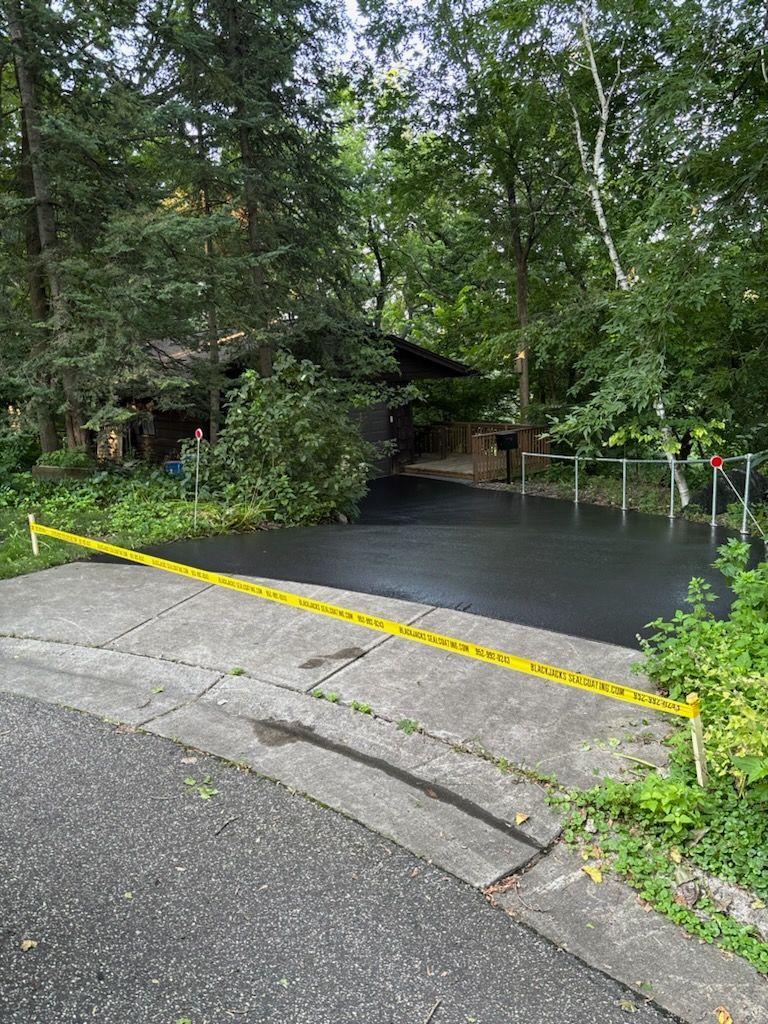 A house is surrounded by trees and has a black driveway.