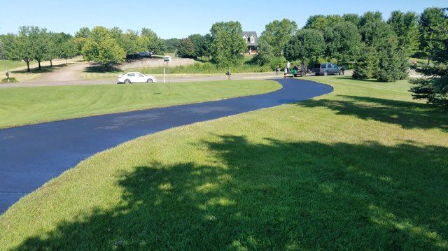 A car is driving down a curvy road next to a lush green field.