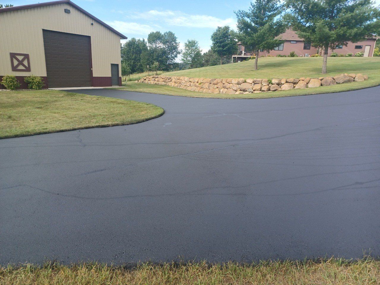 A driveway leading to a house with a barn in the background.