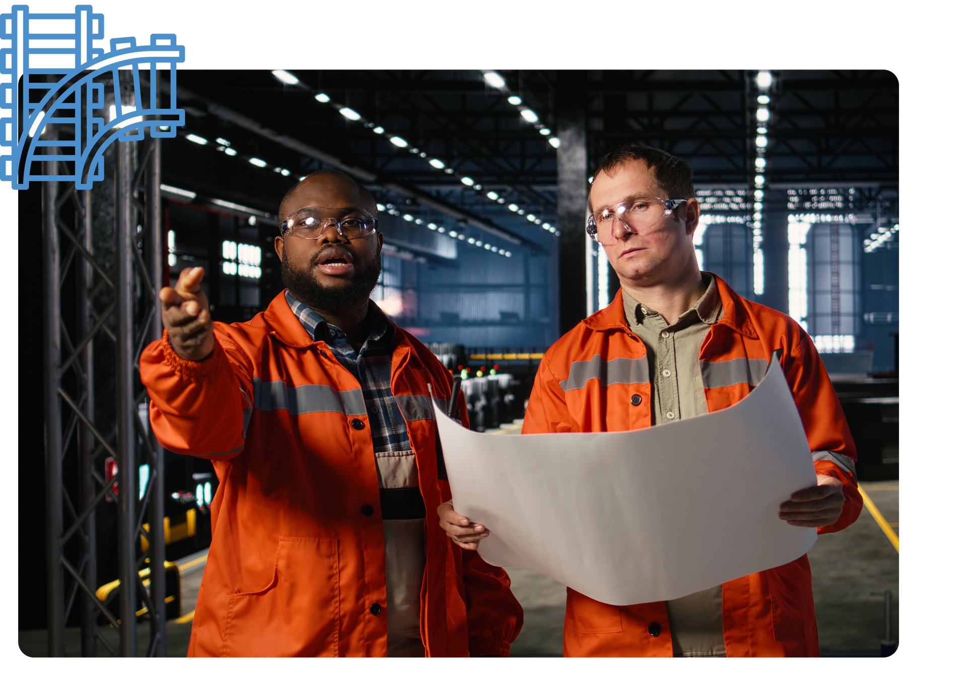 Two people in orange workwear with safety glasses, looking at a blueprint in a factory setting.