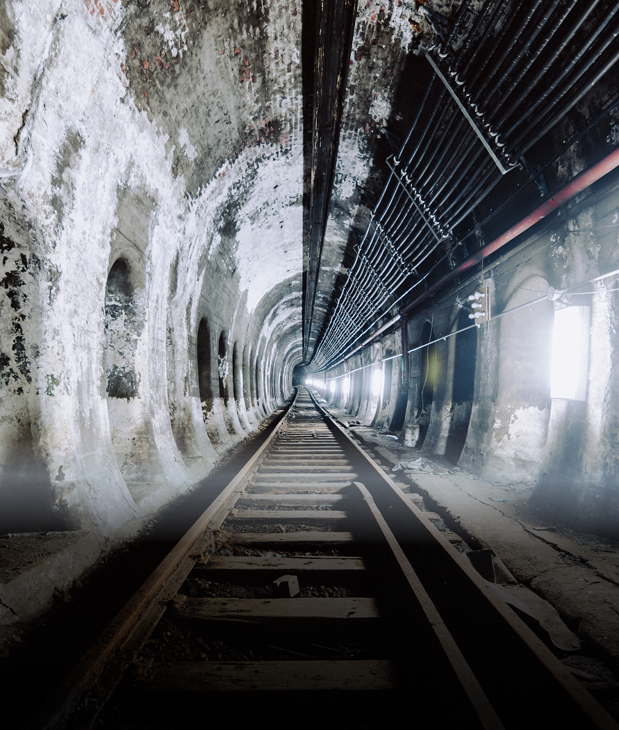 Divided tunnel with railroad tracks. One side appears old and white, the other is dark with cables.