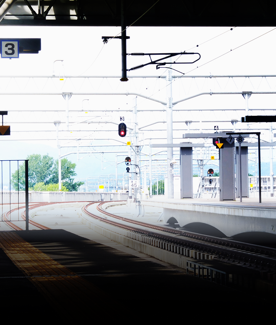 Railroad tracks curving toward a platform under a bright sky, with overhead power lines.