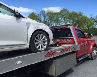 A white car is being towed by a red tow truck.