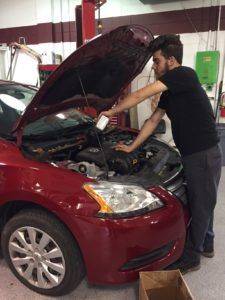 A man is working under the hood of a red car.