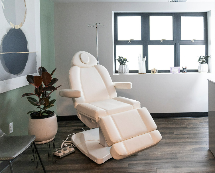 Cream-colored medical chair in a bright room with a large window and potted plants.