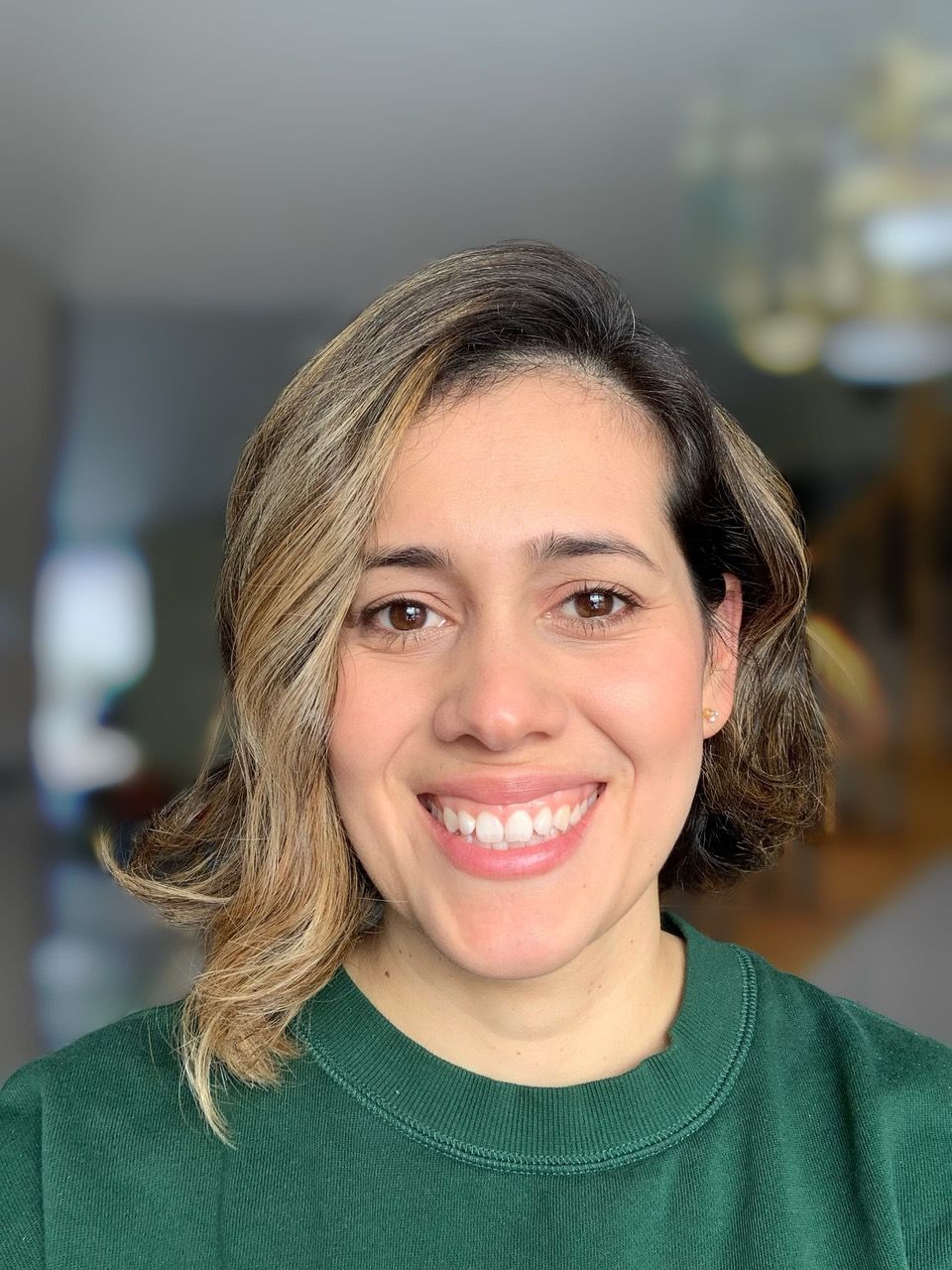 Woman with brown wavy hair smiles, wearing a green sweater.