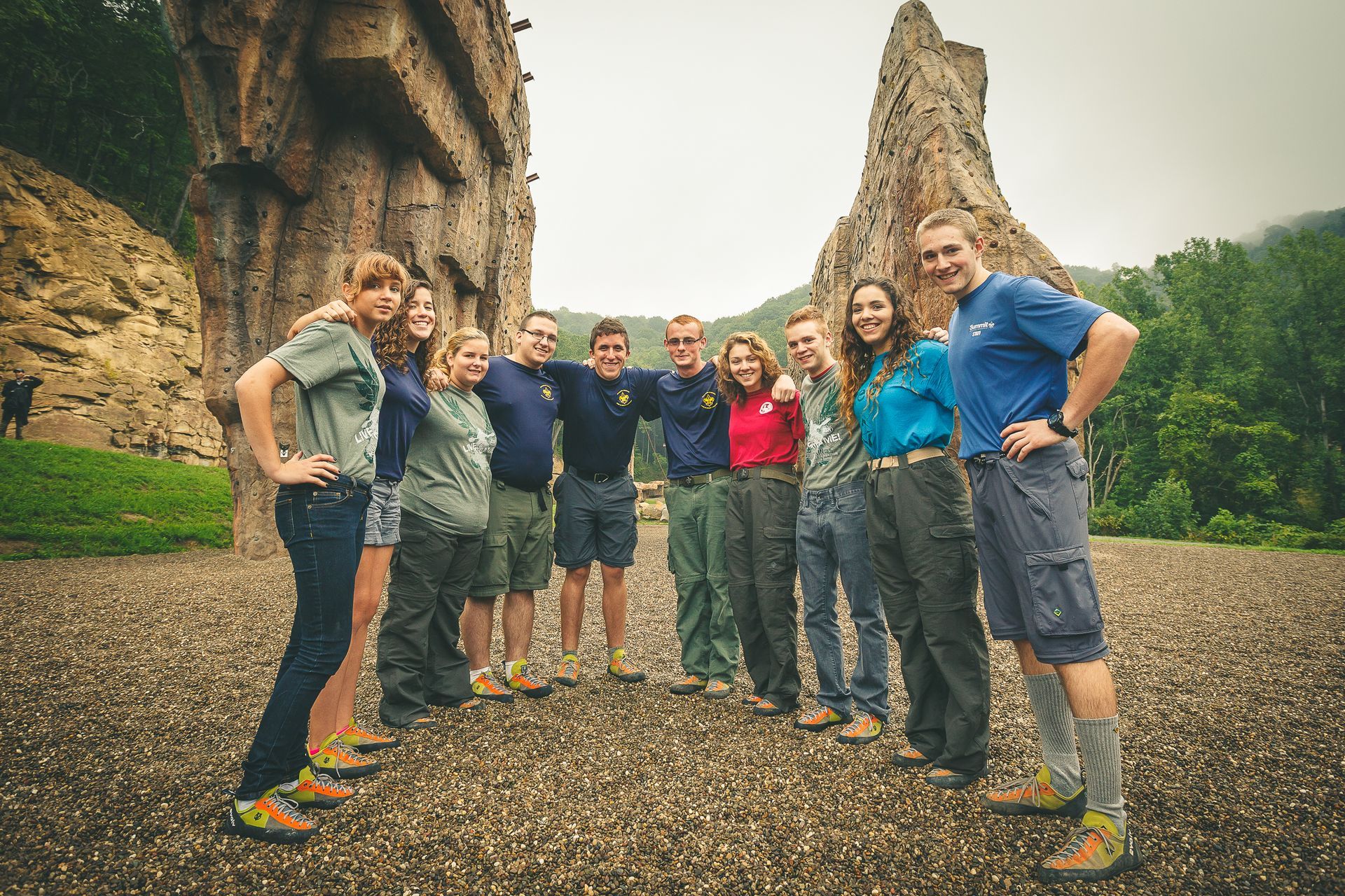 Group of people pose with arms around each other near two large rock climbing walls outdoors.